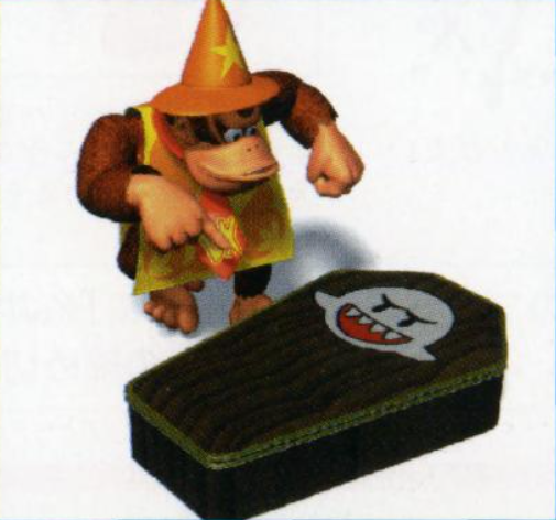 Donkey Kong, wearing a yellow and orange wizard shawl and pointed wizard hat, stands over and points at a coffin. The coffin is emblazoned with the emblem of a Boo.
