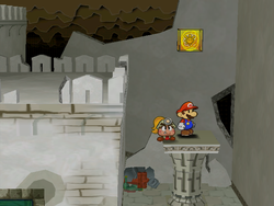 Mario next to the Shine Sprite on the roof of the rightmost column in the center room of level 1 of Rogueport Sewer in Paper Mario: The Thousand-Year Door.