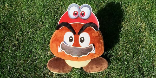 Photograph of a Goomba plushie wearing Cappy and mustache cut-outs