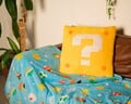 A pillow shaped like a ? Block, and a blue blanket with various Mario entities on it