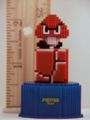 Pixelated figurine of a Goomba standing on top of a Brick Block