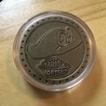 A metal coin featuring an emblem of Cappy, given out by Best Buy as a bonus item for pre-ordering Super Mario Odyssey