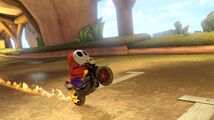 A red Shy Guy, performing a wheelie on its Flame Rider.