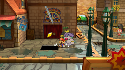 Mario getting the Star Piece under a hidden panel in front of the door to Pianta Parlor in Rogueport's west area in the remake of the Paper Mario: The Thousand-Year Door for the Nintendo Switch.