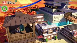 Mario standing near a bell containing five Coins and a Shiny Mushroom in Shogun Studios of The Origami King.