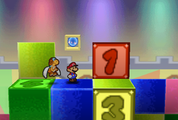 Mario standing next to the Super Block in Shy Guy's Toy Box in Paper Mario.