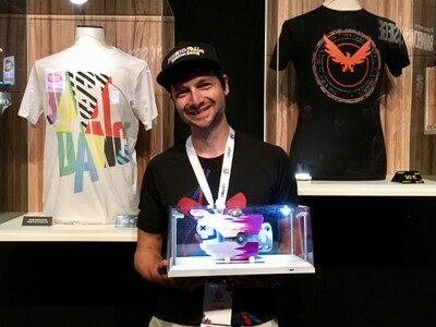 Photograph of Mozsi (also known as "Azzkickah"), winner of the Mario + Rabbids Kingdom Battle Grand Finals, holding his prize: a replica of Rabbid Peach's Comet Blaster. This image was posted by the RabbidsOfficial account on Twitter alongside the following text:Congratulations to Azzkickah, our #MRKBCompetition Grand Champion! Thank you to all the worthy finals competitors and the community for making the competition such an amazing ride at #UbiGamescom.