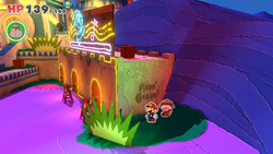 Mario standing near writing on the wall in Shroom City of The Origami King, with a Coin Bag being diggable here.