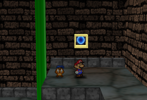 Mario standing next to the Super Block deep in the west area entrance in Toad Town Tunnels in Paper Mario.